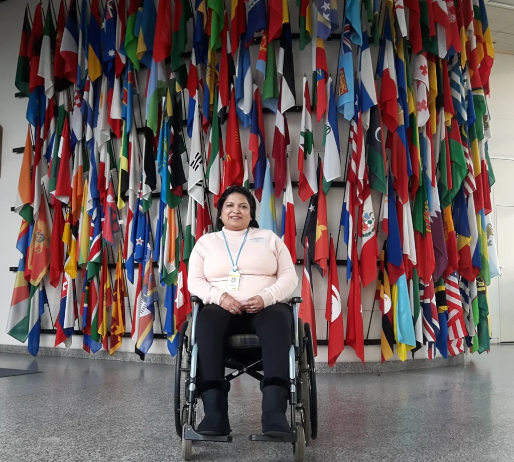 The image shows a woman in a wheelchair is posing for the camera in front of different countries flags.