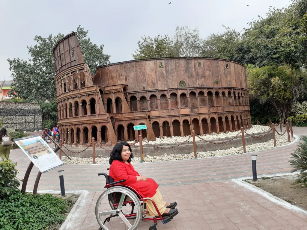 A woman in a wheelchair posing in front of a miniature replica of the Colosseum.