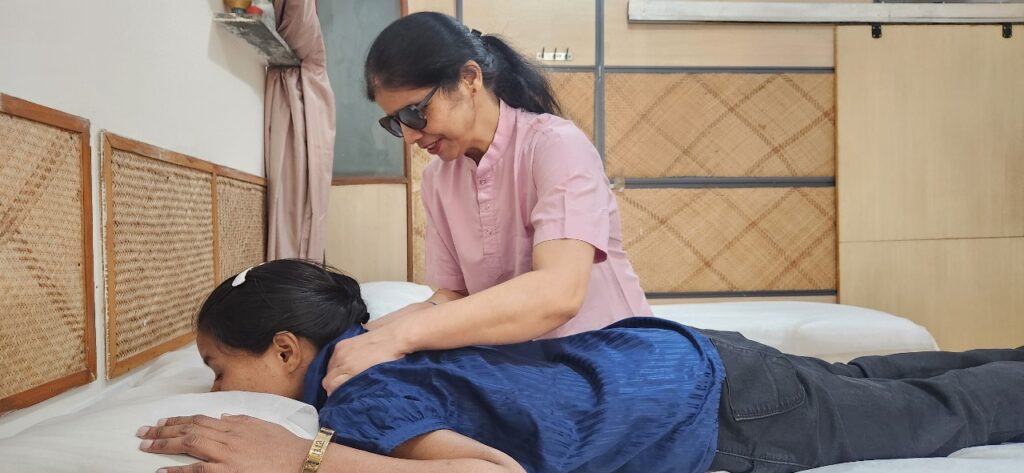 A woman wearing glasses is giving another woman a shoulder massage.