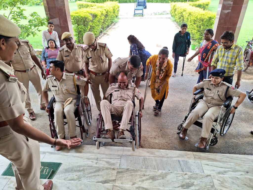 The image shows three police officers, who are in a wheelchair and are trying to climb the steps, with other people in the background that are helping them.