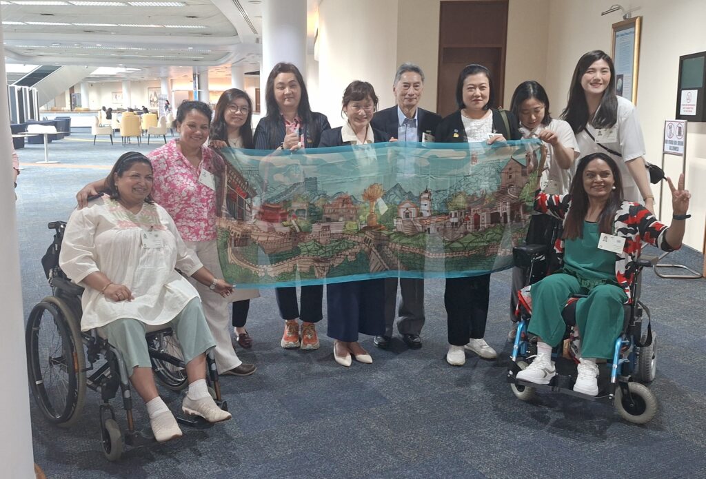 The image shows 10 people in the picture, of which 2 of them are in a wheelchair, and the people are holding a painting and posing for the camera