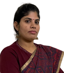 A headshot of Radhika Gopinath, a woman with dark hair pulled back. She has brown eyes and a small red bindi. She is wearing a dark red top and a patterned maroon and gold saree.