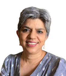 Dr. Kalpana Viswanath, an elder woman with white hair, wearing grey color shirt is smiling at the camera.