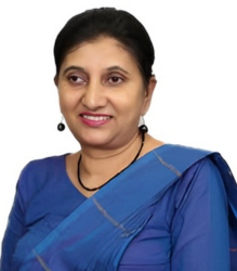 Ms. Manique Gunaratne, is wearing a blue saree with a neat bun and is smiling at the camera.