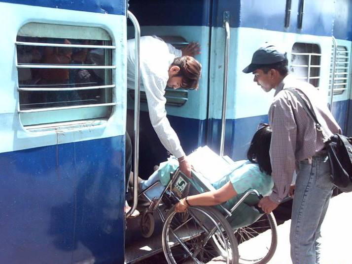 This image shows a woman in a wheelchair being carried by two men that helps her to get in the train.